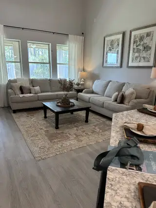 A cozy living room featuring plush sofas, elegant artwork, and a soft rug, with natural light streaming through large windows.