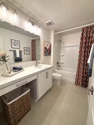 Elegant bathroom featuring a marble countertop, chic lighting, modern art, and a colorful shower curtain.