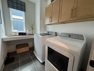A modern laundry room with sleek appliances, light wood cabinets, and a bright window offering natural light.