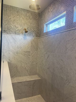 Model Home A luxurious shower with marble tiles, herringbone accents, a built-in bench, and modern rain showerhead.