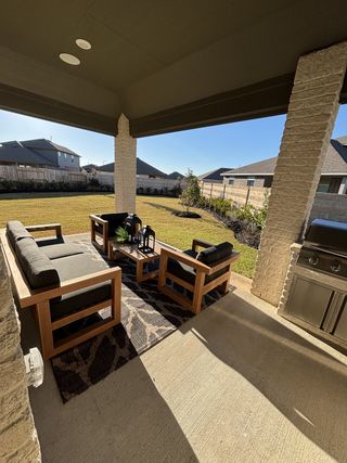A cozy outdoor patio with wooden furniture, a rug, and a grill overlooking a spacious backyard.
