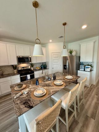 A modern kitchen with granite countertops, white cabinetry, sleek appliances, and elegant pendant lighting.