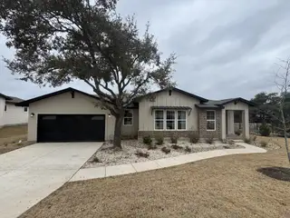Modern single-story home with black garage, large windows, and landscaped front yard with a mature tree.