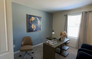 A cozy office space with a sleek desk, globe, and artistic wall art, complemented by natural light from a large window.