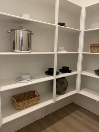 A spacious pantry with sleek white shelving, warm wooden flooring, and organized kitchenware for practical storage.
