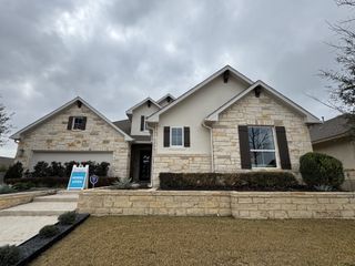 A stunning stone-accented home exterior with dark shutters and a welcoming entry in Veramendi by Scott Felder Homes (New Braunfels, TX).