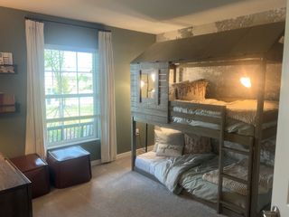 A cozy bedroom featuring a unique bunk bed with rustic design, soft lighting, and a large window with white drapes.