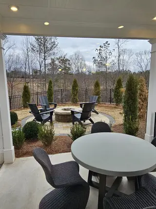 Model Home A cozy covered patio with a seating area and a stone fire pit, perfect for relaxing and enjoying scenic backyard views.