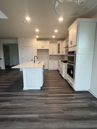 A modern kitchen with sleek white cabinetry, an island, stainless appliances, and wood-look floors. Elegant and spacious design.
