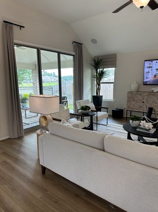 A cozy living area with a light sofa, wooden flooring, and large windows leading to an outdoor patio space.