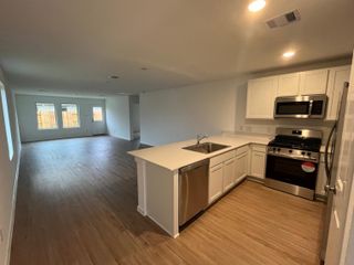 An open-concept kitchen and living area featuring white cabinetry, stainless steel appliances, and warm wood-style flooring.