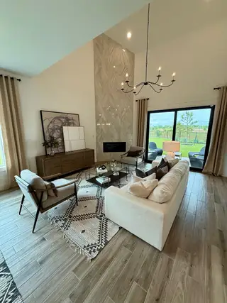 A spacious living room featuring a modern chandelier, stylish furniture, and large windows opening to a lush outdoor view.