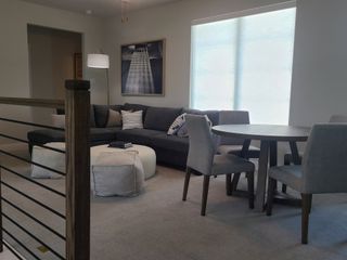 A cozy living area with a sectional sofa, modern artwork, round dining table, and soft natural lighting through a large window.