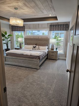 A stylish bedroom with a wood-accented ceiling, plush carpet, and natural light filtering through large windows.
