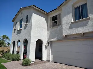 Street view A charming white stucco home with arched entry and shutters in Hawes Crossing Discovery Collection by Taylor Morrison (Mesa, AZ).