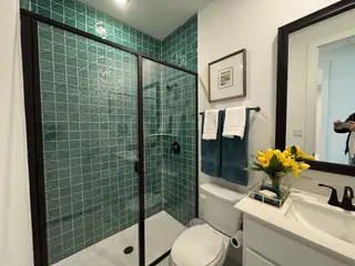 Elegant bathroom with green tiled shower, black fixtures, and a modern vanity.
