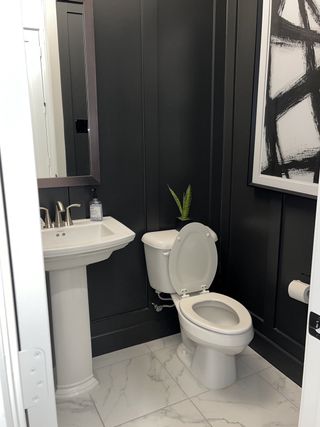 A stylish half-bath with dark accent walls, white fixtures, and modern black-and-white abstract artwork.