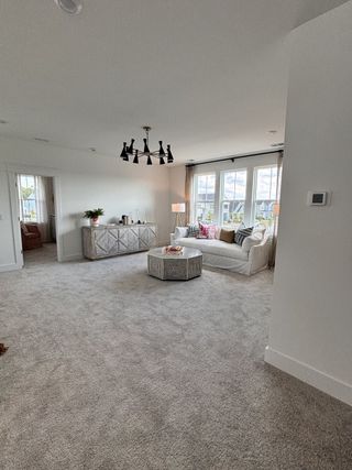 A spacious living area with plush carpet, modern lighting, and large windows, offering cozy seating and a stylish sideboard.