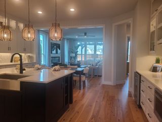 Model Home A modern kitchen with wood floors, stylish pendant lights, and a spacious open layout leading to a cozy living area.