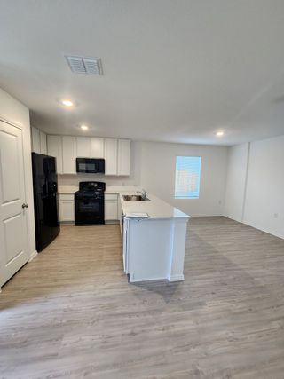 Model Home A modern kitchen with sleek black appliances, white cabinetry, and elegant wood floors, flowing into an open living area.