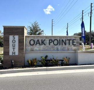 Community Amenities Grand community entrance featuring a stone-accented sign with lush greenery in Oak Pointe by D.R. Horton (Apopka, FL).