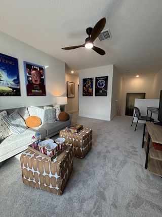 A cozy entertainment room with plush seating, decorative ottomans, movie-themed posters, and soft carpeting.