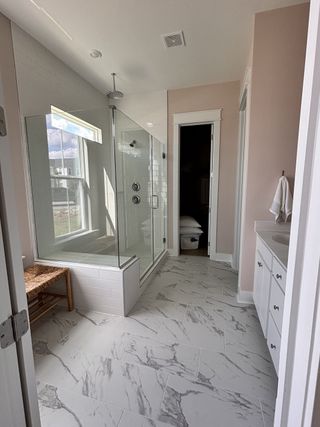 A modern bathroom featuring a spacious glass shower, marble-patterned tiles, and white cabinetry.