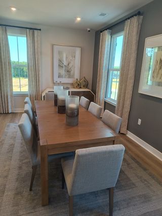 A cozy dining room featuring a wooden table, soft gray chairs, elegant decor, and natural light from large windows.