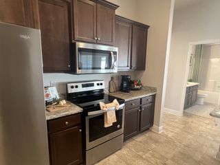 A contemporary kitchen with dark wood cabinets, granite countertops, stainless steel appliances, and tile flooring.