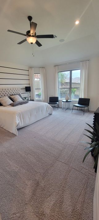 A spacious master bedroom with plush carpeting, a stylish ceiling fan, and large windows, in a Davis Ranch home by Coventry Homes (San Antonio, TX). 