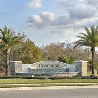 An inviting community entrance with lush greenery, palm trees, and modern signage in Concorde by D.R. Horton (Sanford, FL).
