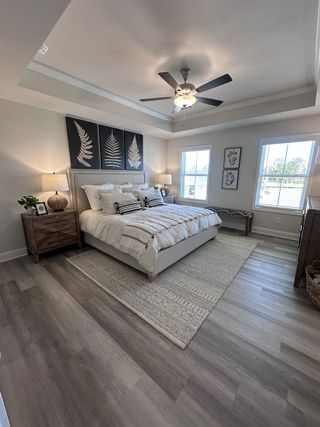 Model Home A cozy bedroom featuring a tray ceiling, elegant artwork, and a neutral color palette with stylish wood flooring.
