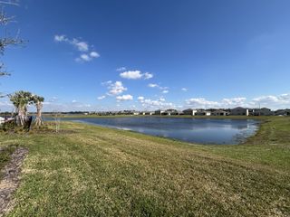 A serene lakeside view in Buena Lago by D.R. Horton, showcasing lush greenery and distant houses in St. Cloud, FL.
