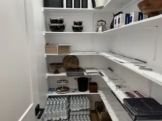Model Home A well-organized pantry with sleek white shelves, stocked with kitchenware, bottles, and neatly arranged documents.
