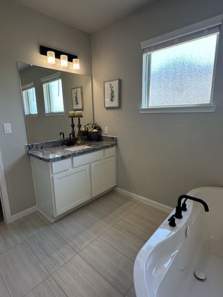 A sleek bathroom featuring a granite countertop, elegant lighting, and a relaxing bathtub with modern black fixtures.