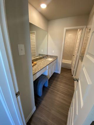 Model Home A modern bathroom with granite countertops, spacious mirror, and wood-style flooring for a sleek, inviting look.