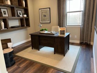 A cozy office with a dark wood desk, built-in shelving, and natural light filtering through sheer curtains.