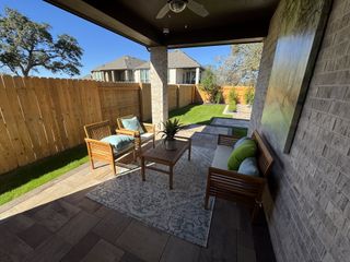A cozy covered patio furnished with stylish wooden seating, providing a comfortable space to enjoy the lush backyard landscaping and stone-paved firepit area.