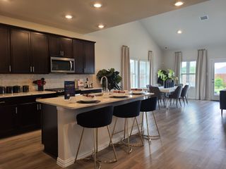 Model Home A modern kitchen and dining area with dark cabinets, sleek appliances, and wood flooring, leading to a bright, airy space.
