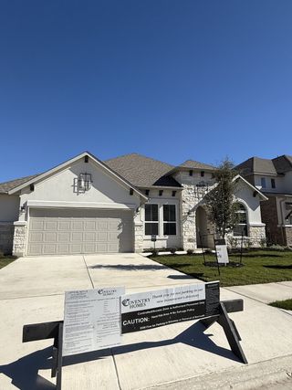 Street view A modern stone-brick home with a neat lawn in Carneros Ranch by Coventry Homes (Leander, TX).