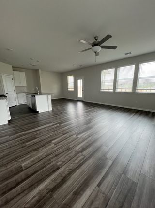 An open-concept living space with dark wood-look flooring, a ceiling fan, and abundant natural light from large windows.