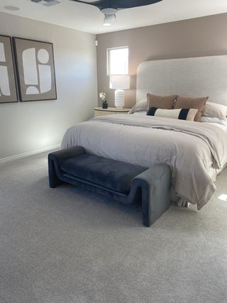 A serene bedroom with plush gray carpet features a tufted headboard, neutral bedding, and a stylish velvet bench, creating a tranquil retreat.
