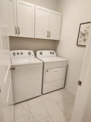 Compact laundry room with white cabinets, washer, and dryer on sleek tiled floor; a functional and clean design.