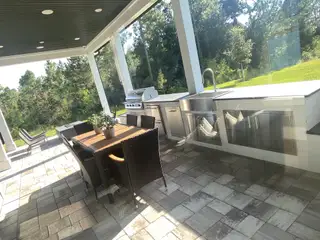 A spacious outdoor kitchen with a sleek countertop, grill, and dining area overlooking lush greenery.