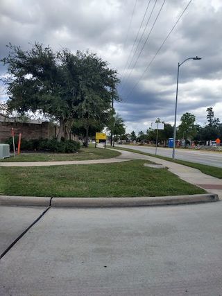 A welcoming neighborhood entrance in Lakewood Pines Trails by KB Home (Houston, TX), lined with lush greenery.