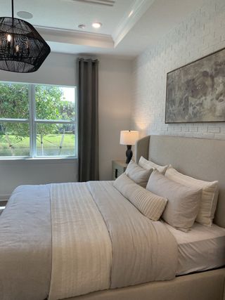 A serene bedroom featuring a cozy bed, textured white brick wall, and modern pendant lighting, overlooking a lush green view.