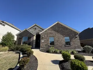 Street view A charming brick home with manicured landscaping in the Sunfield community by Brightland Homes (Buda, TX).