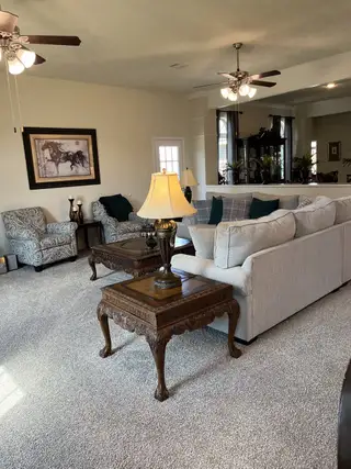 A spacious living room with plush seating, ornate wooden tables, stylish art, and ceiling fans.