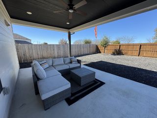 A cozy patio with a stylish outdoor sectional, ceiling fan, and fenced backyard, perfect for relaxing and entertaining.