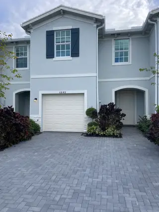 Street view A charming blue home with white trim and a brick driveway in Lakeshore at The Fountains by Lennar (Lake Worth, FL).